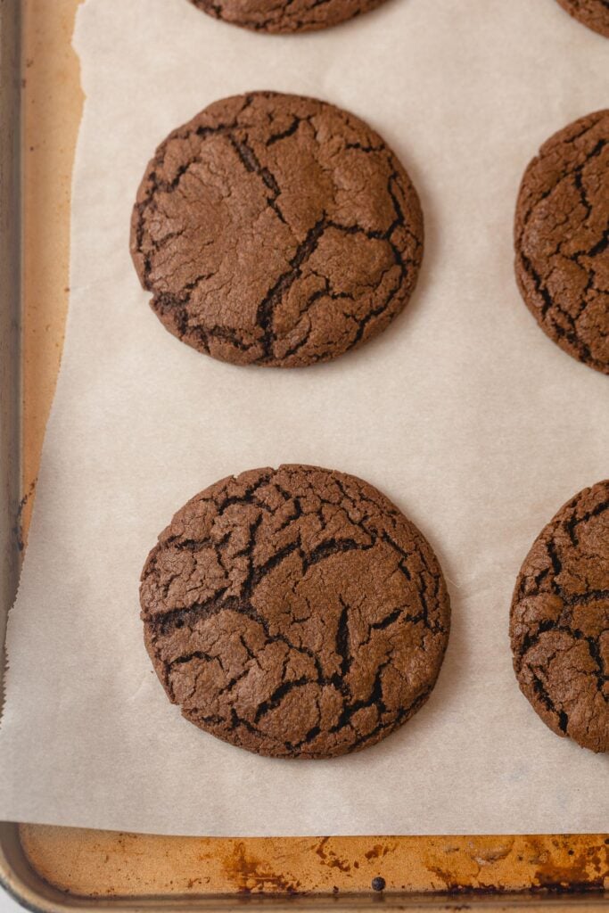 Crackled chocolate cookies on parchment-lined baking sheet.