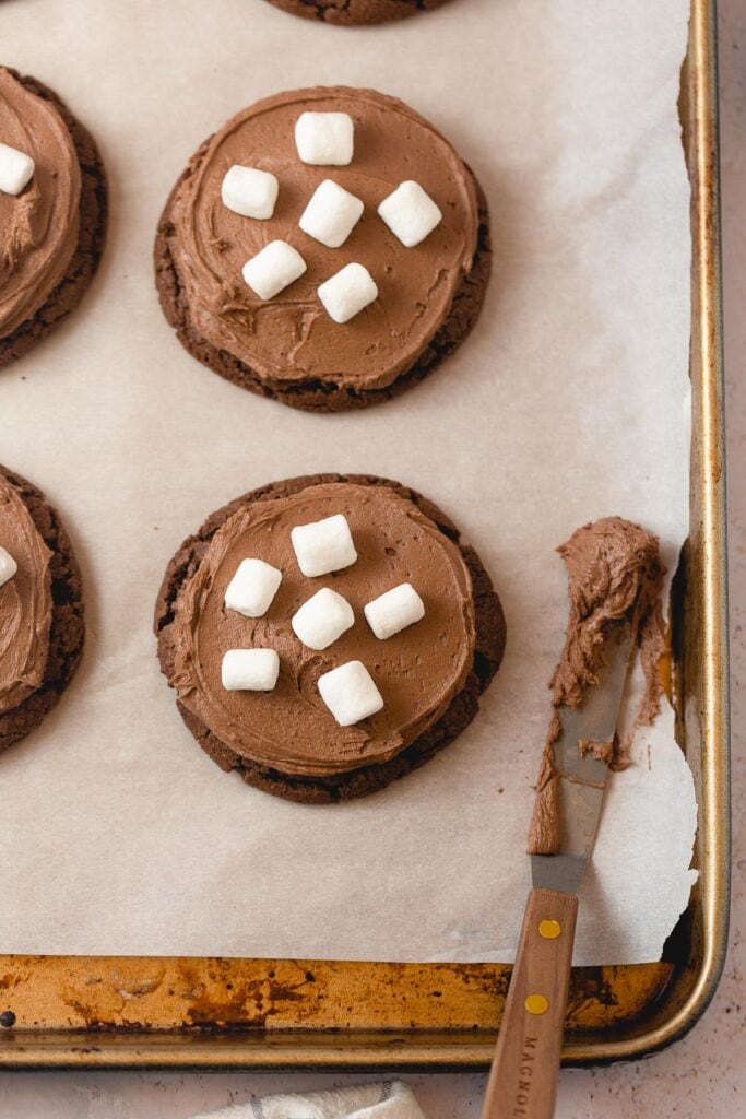 Chocolate cookies with chocolate frosting and marshmallows on a baking sheet.
