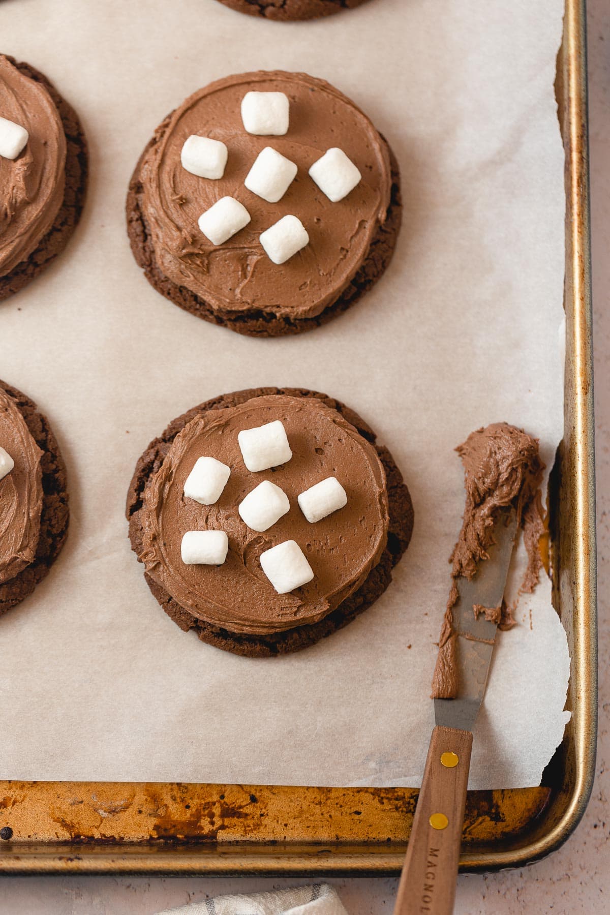 Chocolate cookies with chocolate frosting and marshmallows on a baking sheet.
