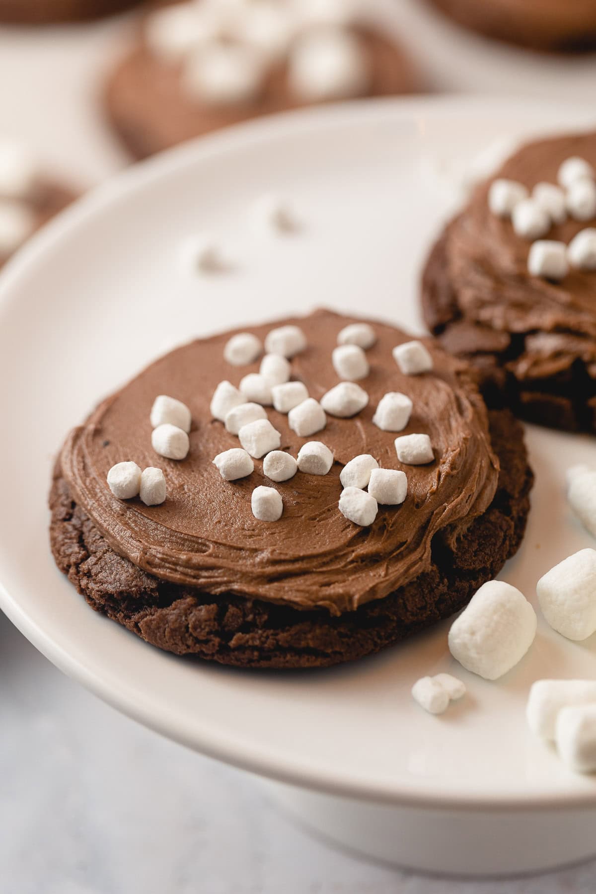 A cake stand with chocolate cookies frosted with chocolate frosting and micro marshmallows.