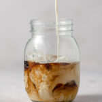 Swirling creamer and coffee in a glass mason jar.