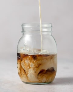 Swirling creamer and coffee in a glass mason jar.
