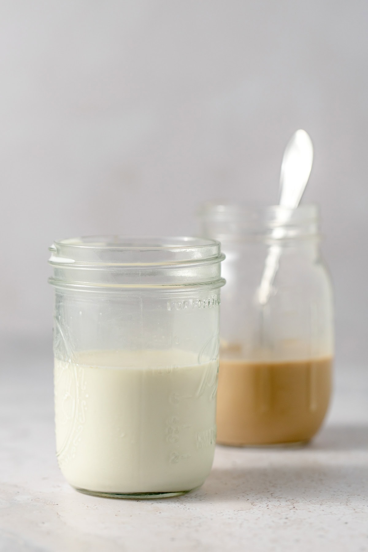 A mason jar of heavy cream mixed with milk and sugar with a mason jar filled with iced coffee behind it.