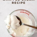 A spoon filled with whipped cream resting on top of a glass measuring cup filled with more whipped cream with the words, "Small Batch Whipped Cream Recipe".