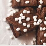 Frosted brownies decorated with mini marshmallows and cut into squares with the words, "Frozen Hot Chocolate Brownies".