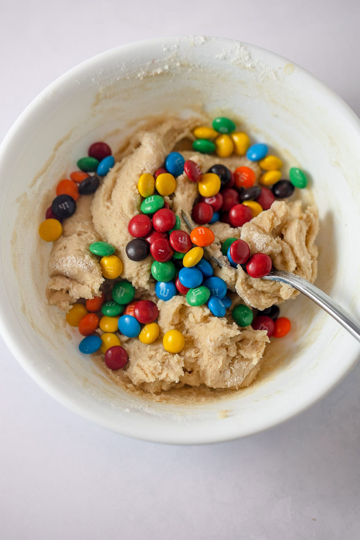 Cookie dough in a white bowl with colorful miniature candy-coated chocolate bits on top.