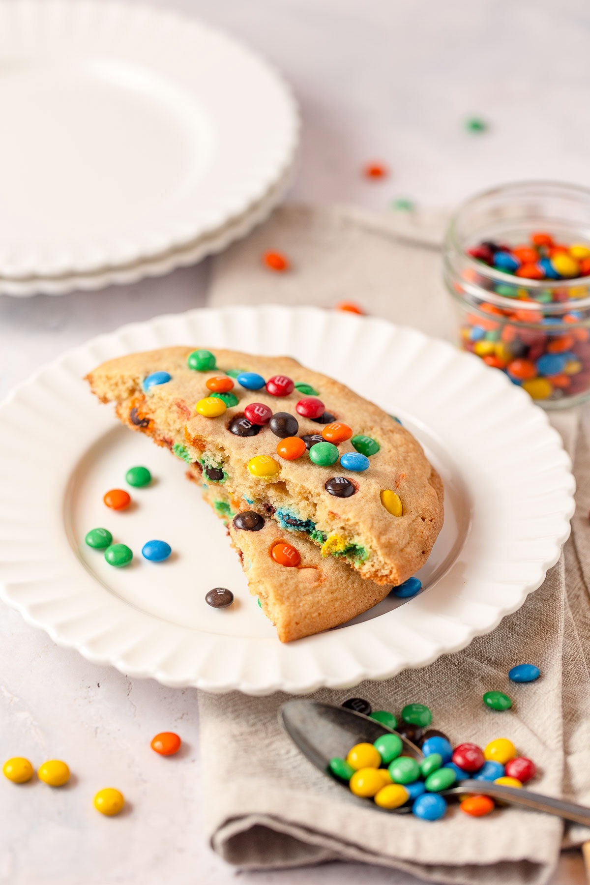 A single M&M cookie split in half and stacked on a white plate with more mini M&Ms surrounding.