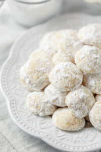 A white plate filled with small powdered sugar dusted cookies.