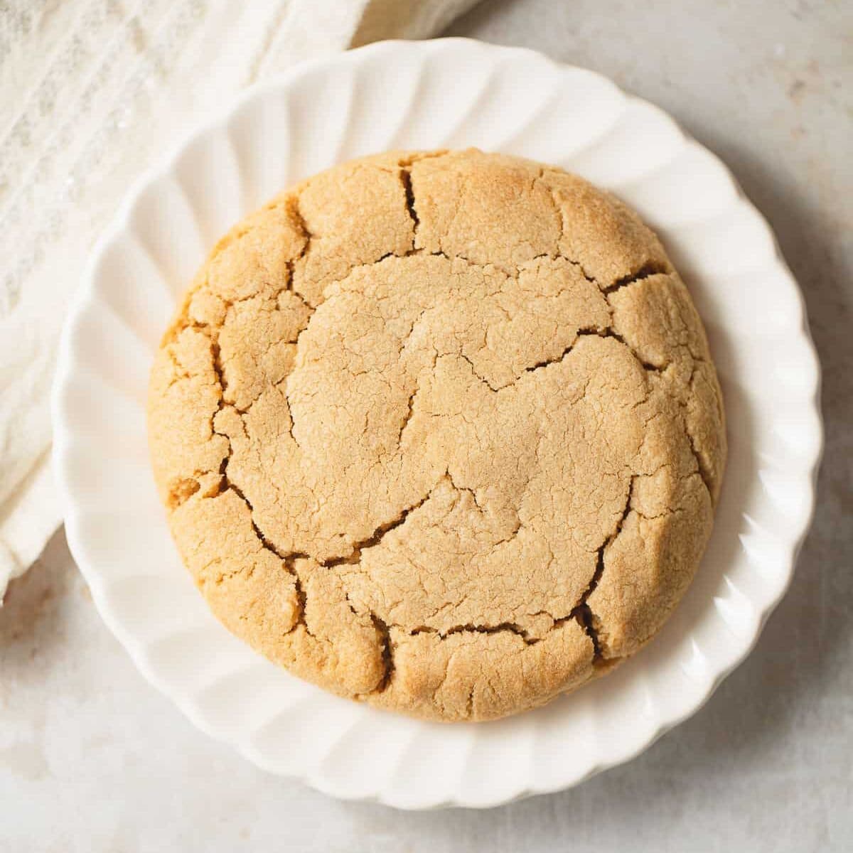 A single peanut butter cookie on a white scalloped plate.